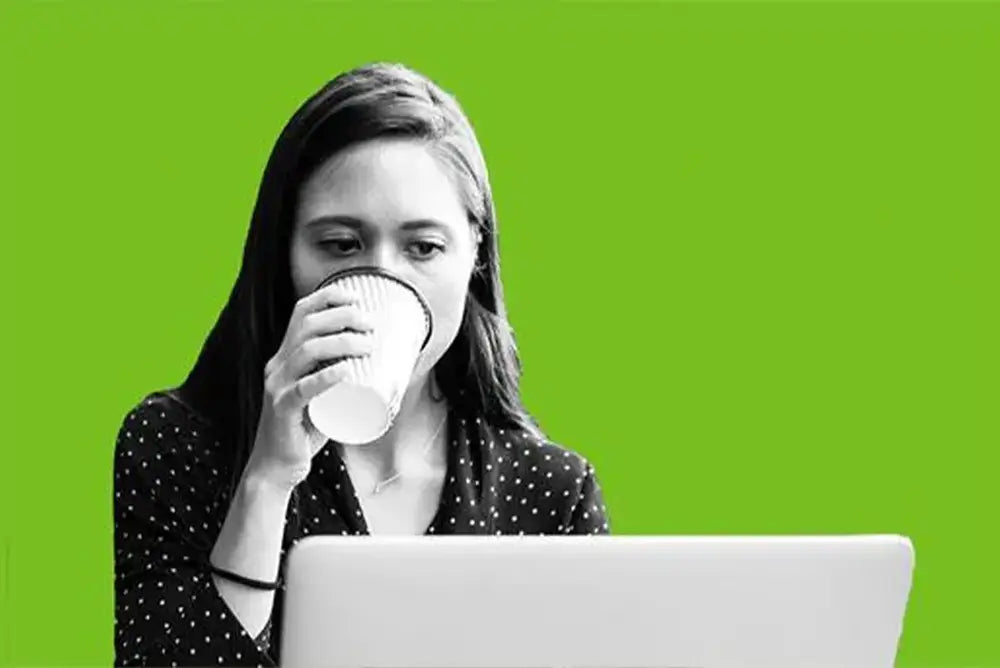 A woman drinking coffee in front of a laptop