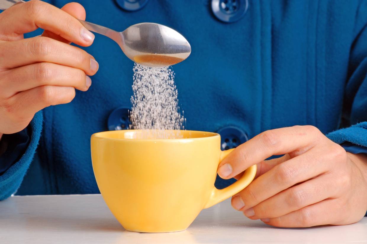 man pouring a lot of sugar into a mug